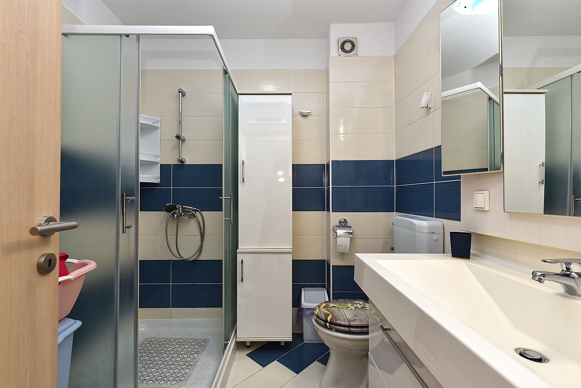 Um banheiro moderno com box de vidro, vaso sanitário com assento decorativo e pia com espelho acima.
