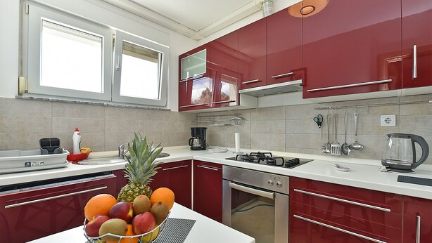 A modern kitchen with red cabinets, a stainless steel stove, and a fruit bowl on the counter. - Apartment 2333/111878 (Istria - Pula), 3000m from the beach (Pula)