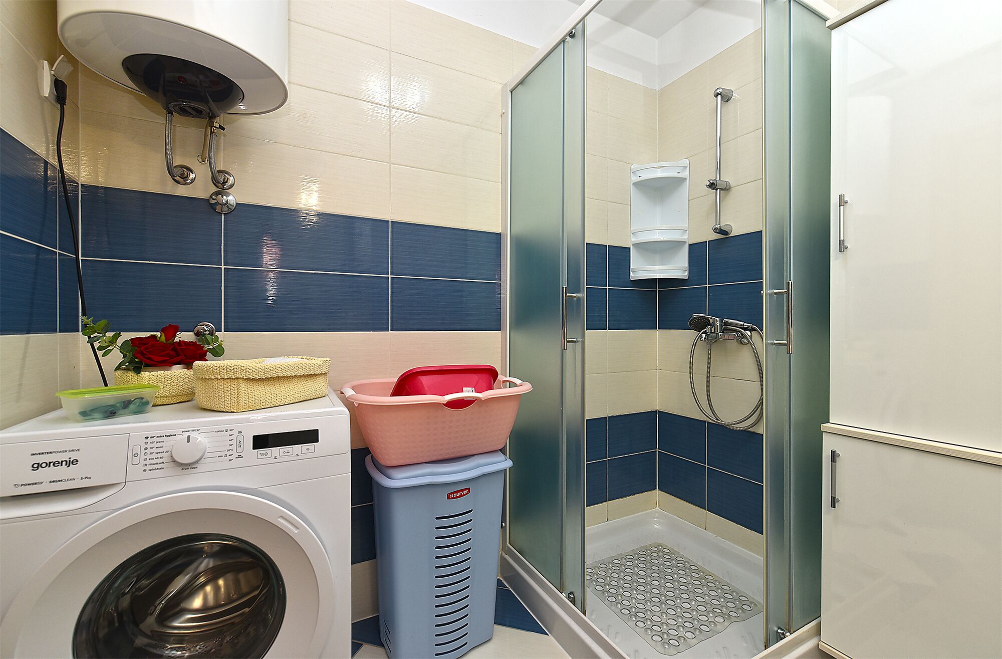 Une petite salle de bain équipée d’un lave-linge, d’une douche à parois de verre et d’un mur recouvert de carreaux.