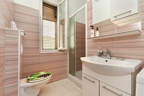 A bathroom with striped walls, a toilet, a sink, and a shower.