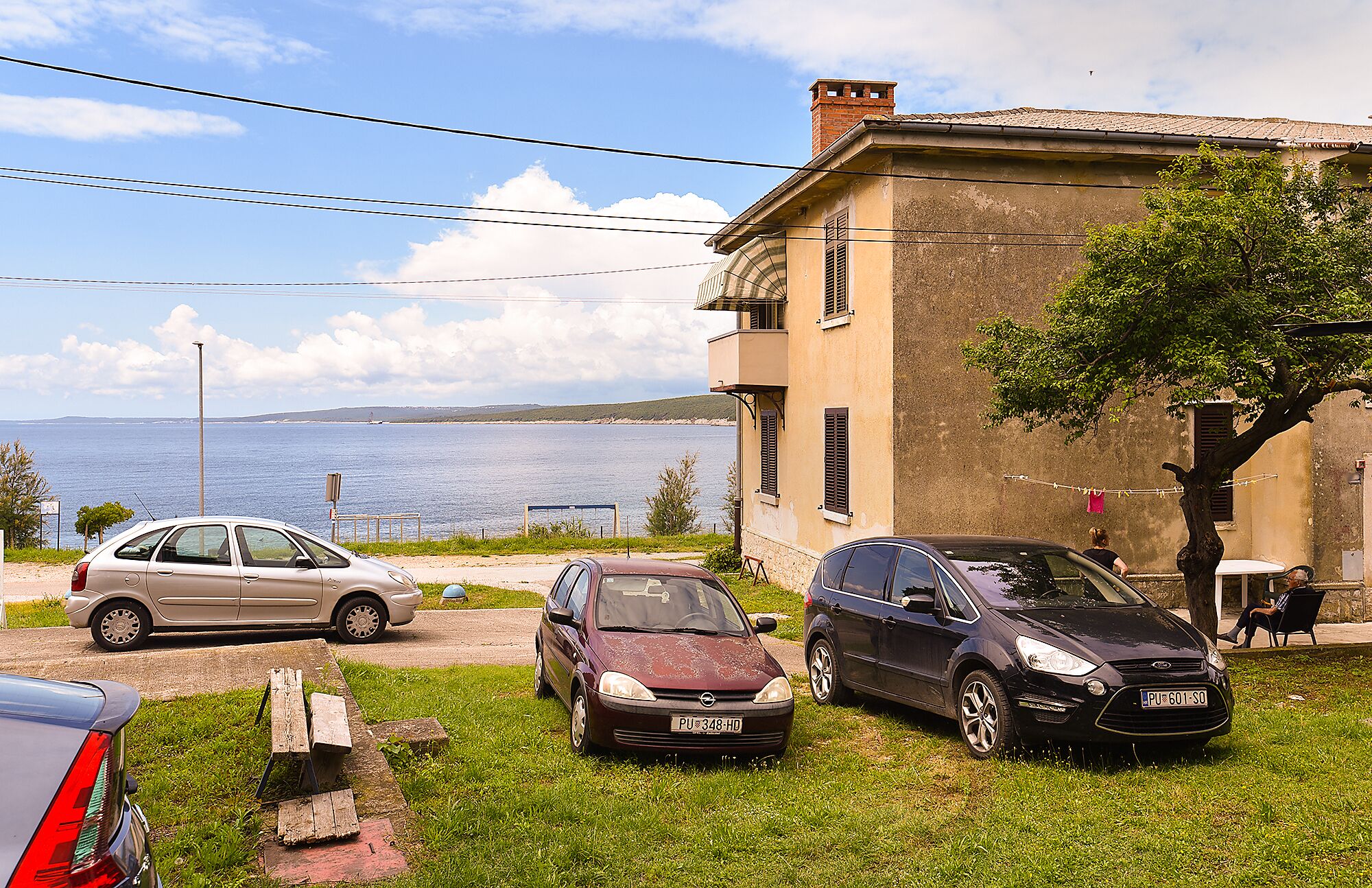 Una proprietà costiera con auto parcheggiate, un tavolo da picnic e vista sul mare.