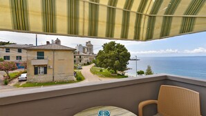 Un balcón con vistas a un pueblo costero, una mesa con una vela azul y una silla de mimbre.