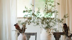 Een eettafel met twee witte vazen met gedroogde planten, een rieten hanglamp en donkerhouten stoelen.
