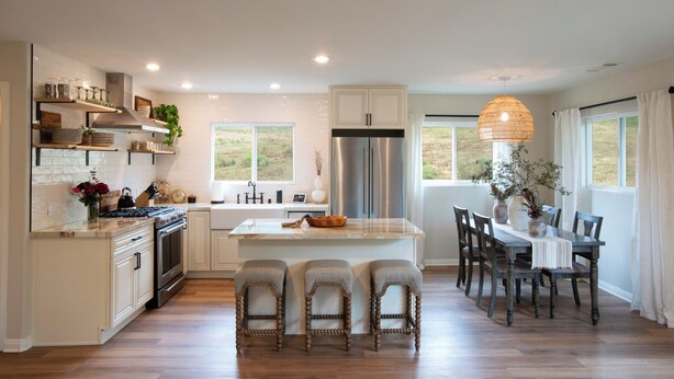 Een moderne keuken met een centraal eiland, barkrukken en een eettafel met stoelen.