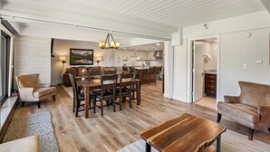 Ampla sala de estar com uma mesa de jantar, sofás e cozinha ao fundo.