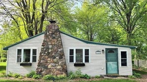 Une petite cabane à un seul étage, avec une cheminée en pierre, un revêtement extérieur blanc et une porte verte.