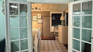 Un couloir étroit avec un sol à motifs, des poutres en bois au plafond et un lit doté d’une tête de lit blanche.