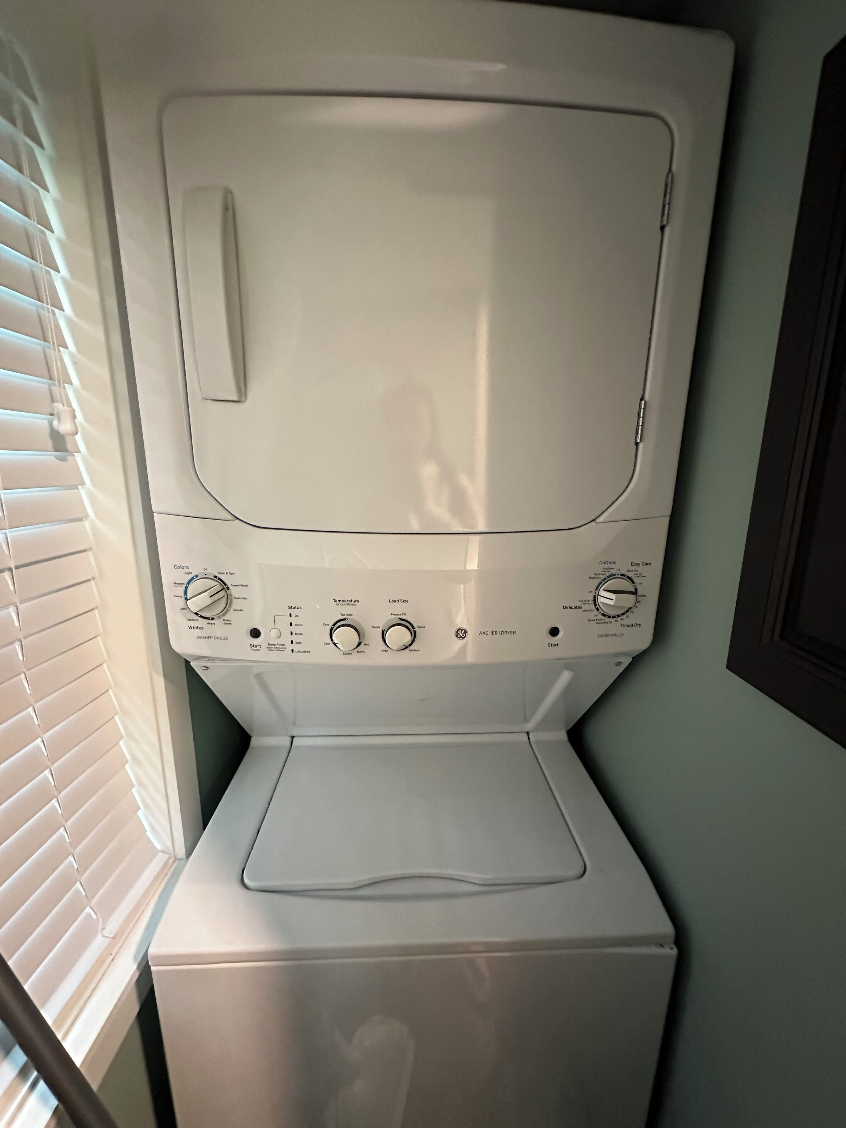 Un appareil combiné lave-linge et sèche-linge à chargement frontal, doté de boutons de commande, d’un bouton de démarrage et d’une étiquette indiquant qu’il s’agit d’un appareil de la marque GE.
