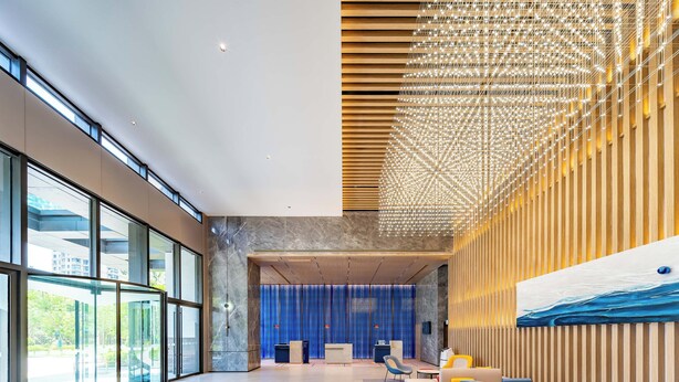 Un'ampia hall con grandi vetrate, un moderno lampadario e un'area salotto con poltrone colorate.