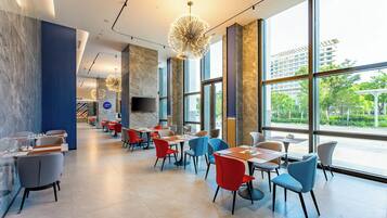 Um restaurante moderno com grandes janelas, diferentes opções de assentos e um lustre central.