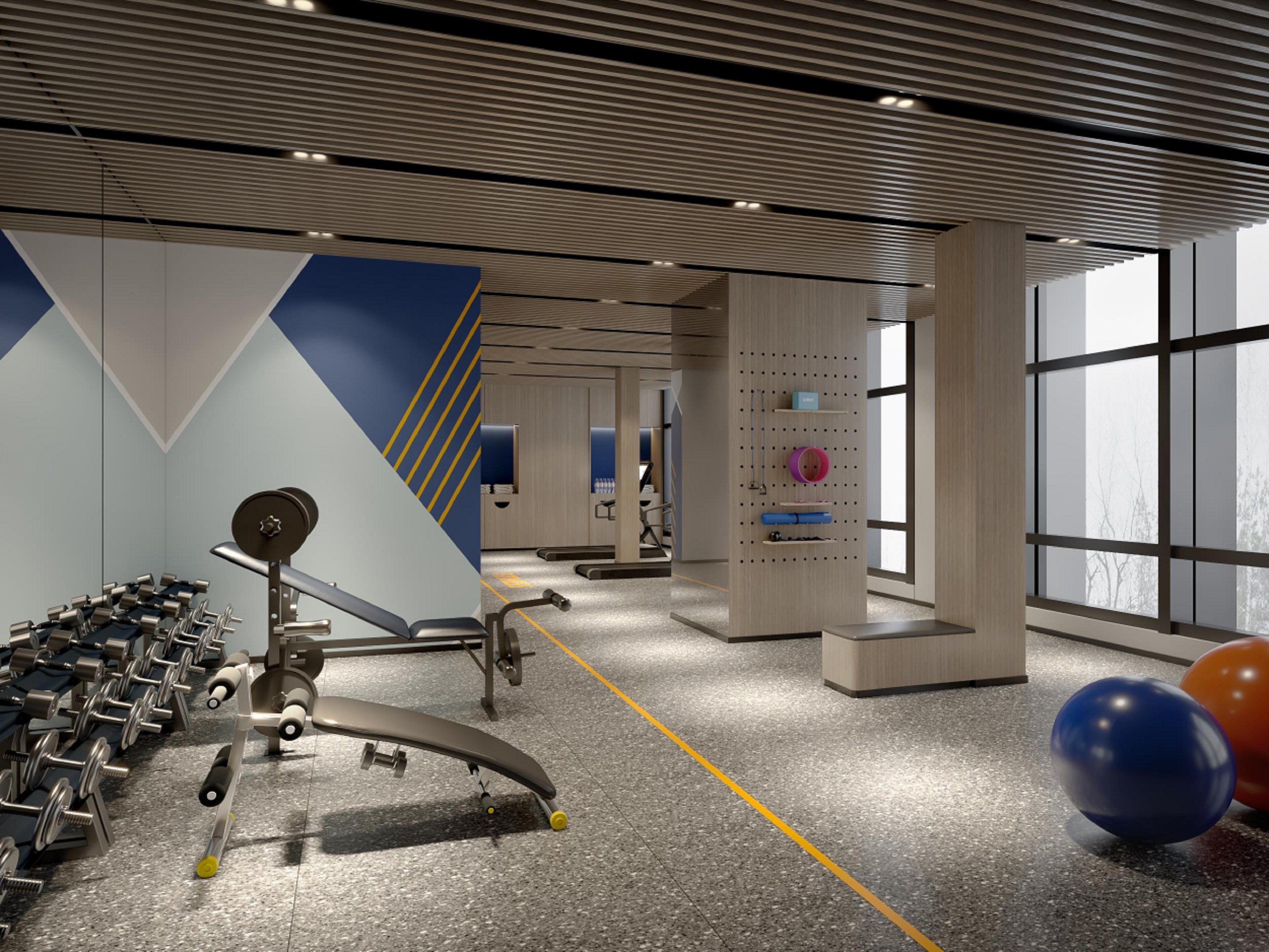 A gym with exercise equipment, a wall with a geometric design, and large windows.