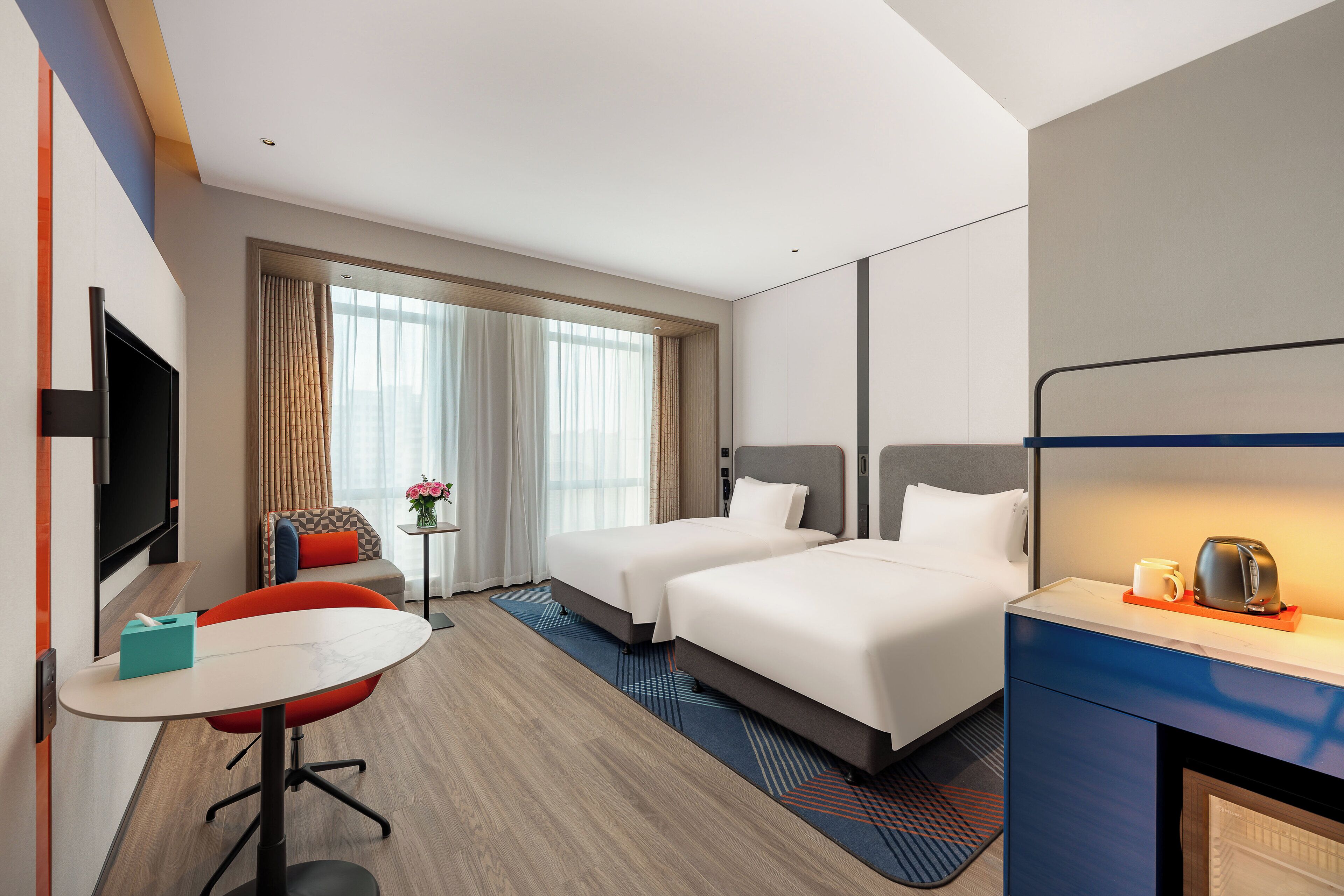 Habitación de hotel con dos camas, un escritorio con silla, televisión y cafetera sobre el escritorio.