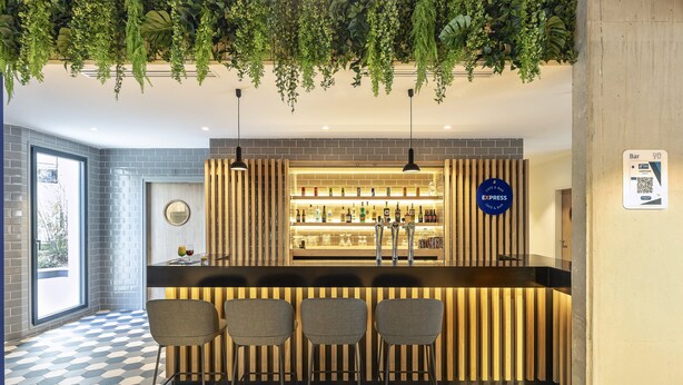 A bar area with a checkered floor, bar stools, and a variety of bottles. - Holiday Inn Express Paris Poissy by IHG (Poissy)