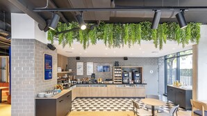 A modern cafe with a checkered floor, wooden furniture, and hanging plants. - Holiday Inn Express Paris Poissy by IHG (Poissy)