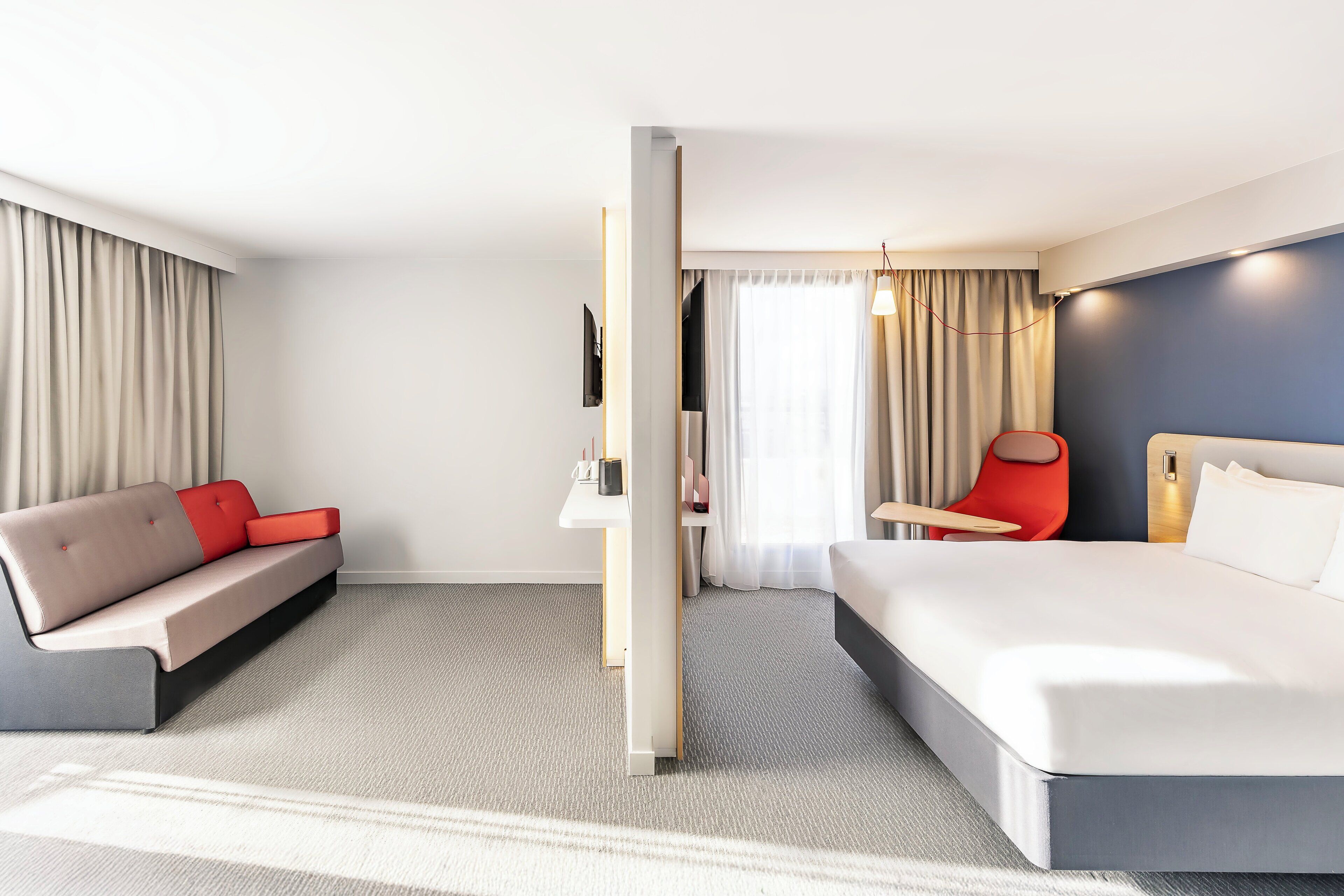 A modern hotel room with a large bed, a sofa, a desk, and a chair.