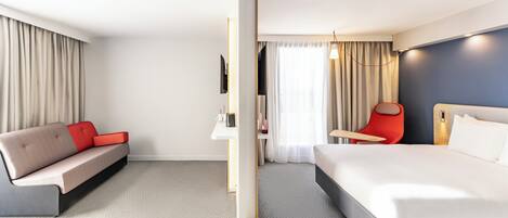 A modern hotel room with a large bed, a sofa, a desk, and a chair.