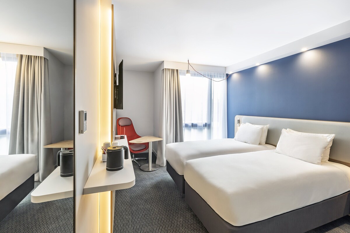 A modern hotel room with two beds, a desk, a chair, and a TV.