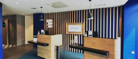 Un área de recepción con dos mostradores de madera, una alfombra azul y un televisor montado en la pared.