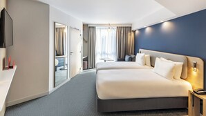 A modern hotel room with a large bed, a desk, a TV, and a view of the city through the window. - Holiday Inn Express Paris Poissy by IHG (Poissy)