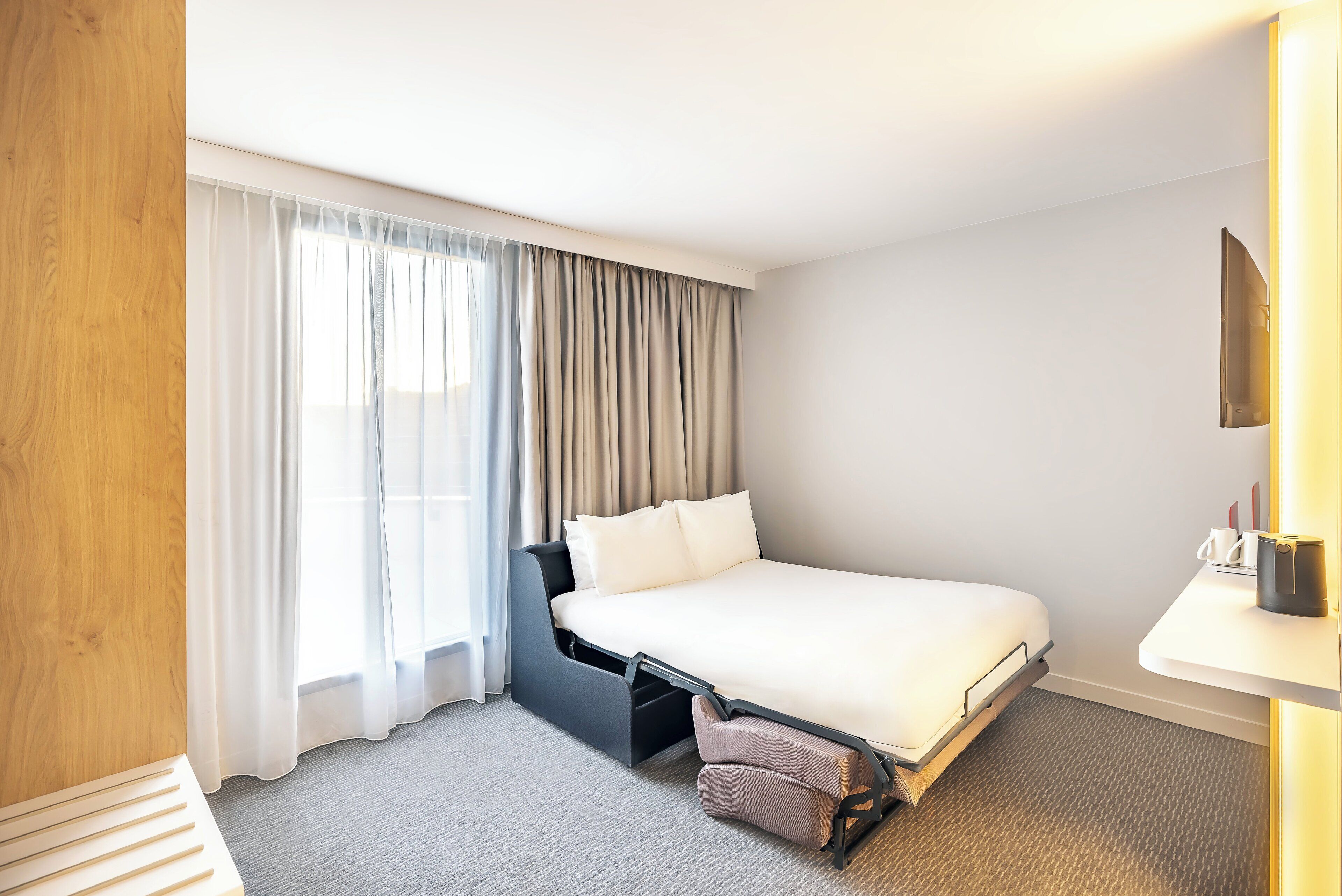 Une chambre d’hôtel moderne, équipée d’un lit, d’un bureau et d’une grande fenêtre avec des rideaux.