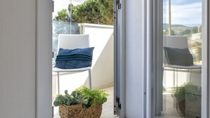 Ein Balkon mit weißem Stuhl, blauem Kissen und einem gewebten Korb mit Pflanzen.