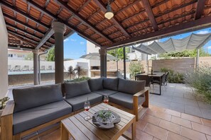 An outdoor seating area with a wooden table, a cushioned sofa, and a pool in the background. - Villa Above by Istrabook (Medulin)