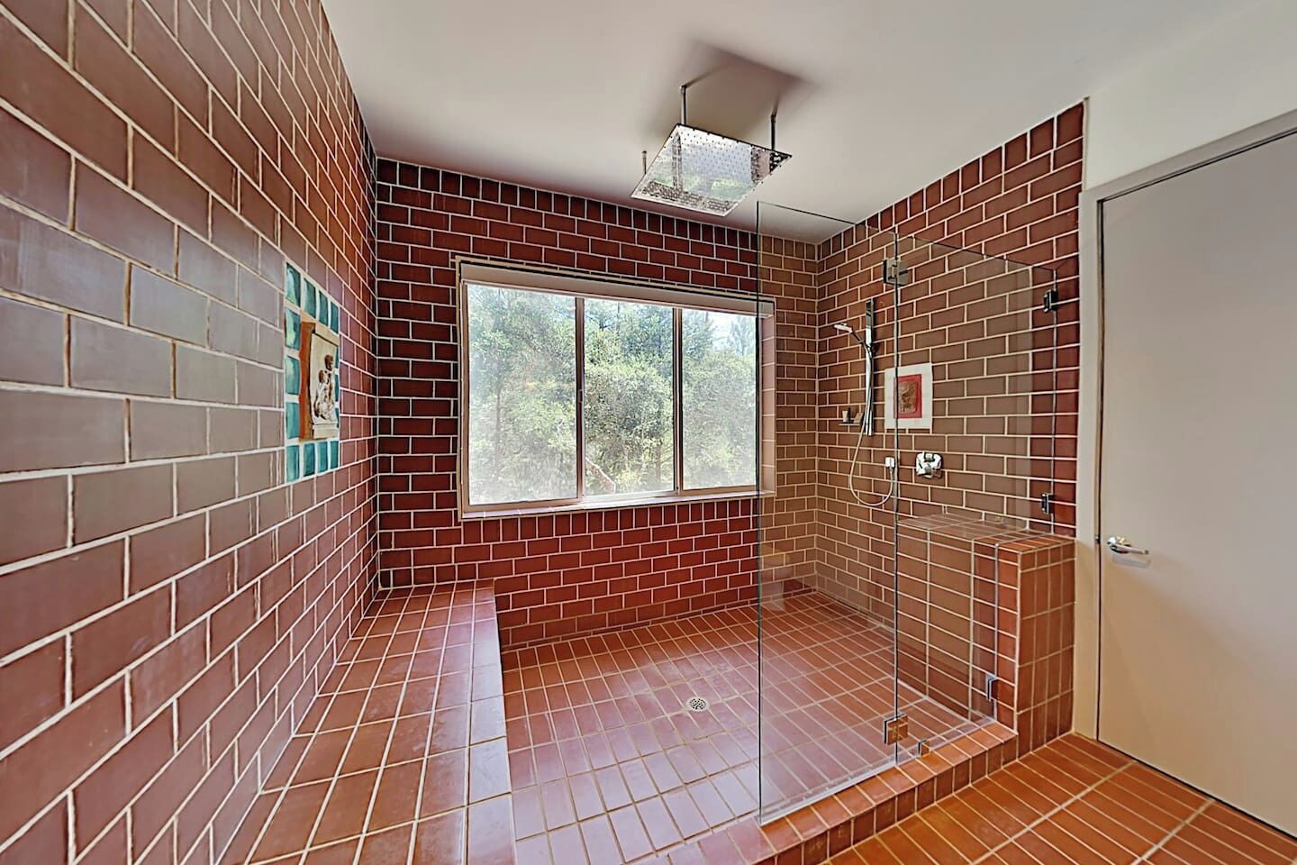 A bathroom with red brick walls, a large window, and a shower area.