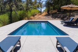 Une piscine rectangulaire avec deux chaises longues et un parasol d’un côté.