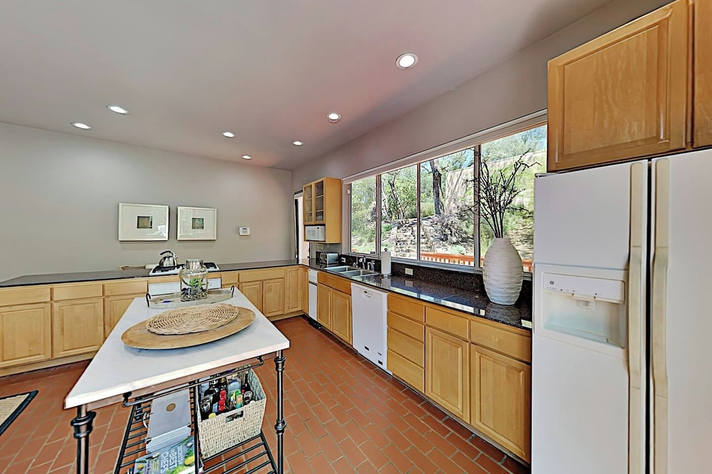 Une cuisine avec des meubles de rangement en bois, un plan de travail blanc, une grande fenêtre et un réfrigérateur.