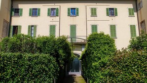 A building with multiple windows, a central entrance, and a pathway flanked by hedges. - Loft Venere - MyHomeinComo (Como)