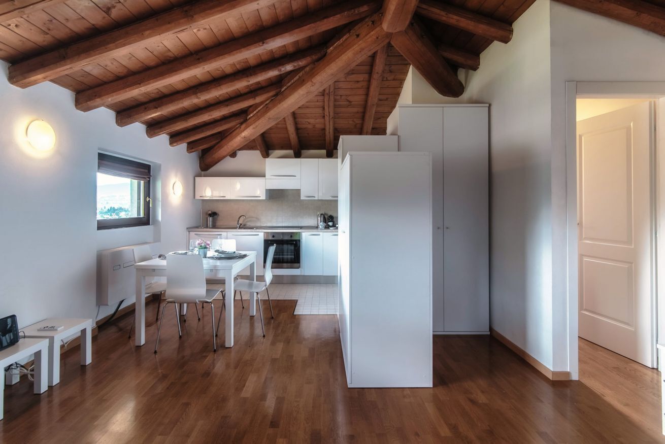 Een moderne keuken met witte kasten, een eethoek met een witte tafel en stoelen, en een houten plafond.