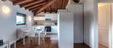 Een moderne keuken met witte kasten, een eethoek met een witte tafel en stoelen, en een houten plafond.