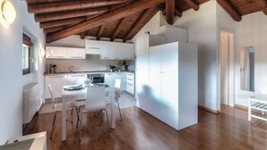 A modern kitchen with white cabinets, a dining area with a table and chairs, and a wooden ceiling. - Loft Venere - MyHomeinComo (Como)