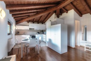 A modern kitchen with white cabinets, a dining area with a table and chairs, and a wooden ceiling. - Loft Venere - MyHomeinComo (Como)