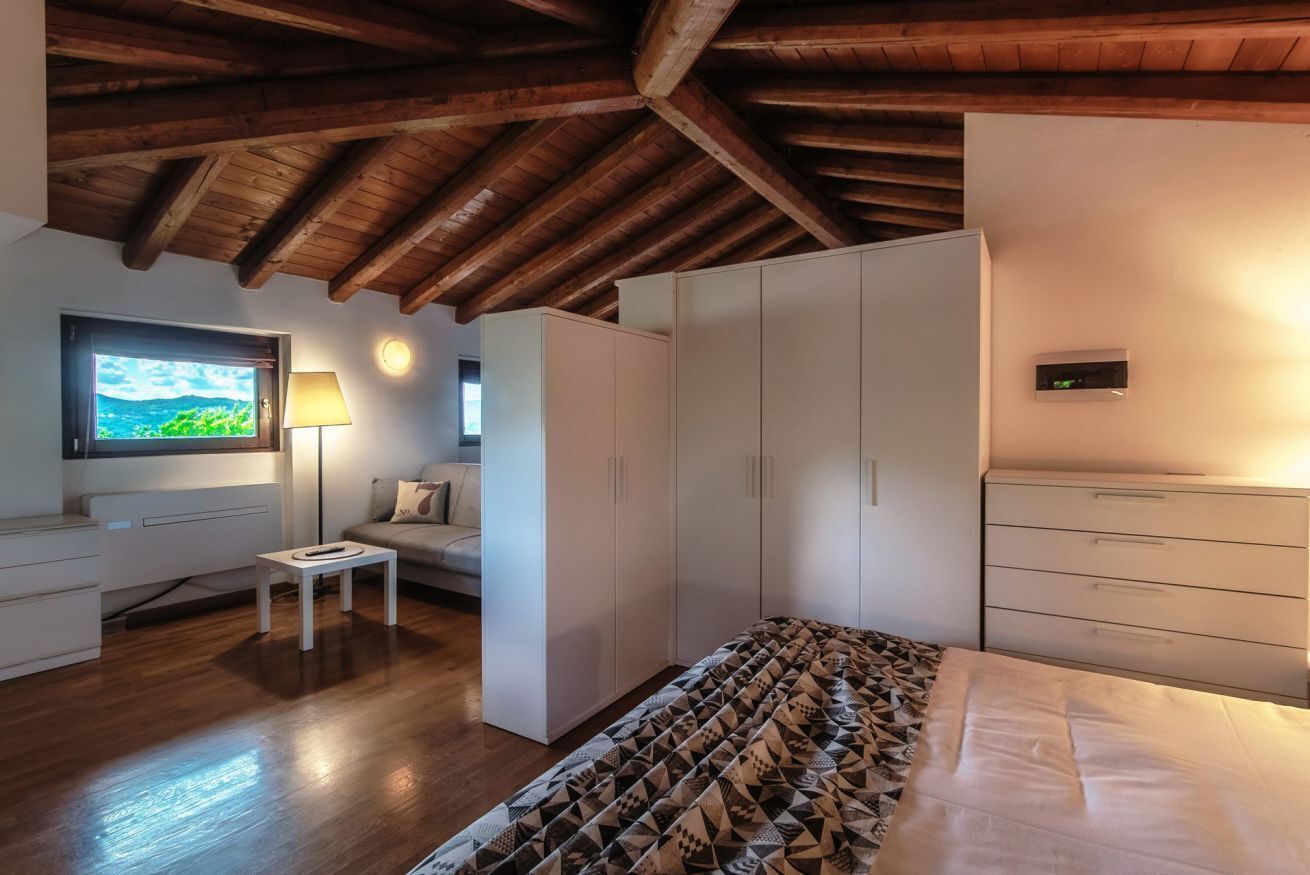 Ein Schlafzimmer mit Holzboden, einem Bett mit gemustertem Überwurf, einem Fernseher, einer Lampe und einem Kleiderschrank.