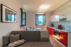 Een moderne keuken met rode kastjes, een eethoek met tafel en stoelen, en een bank met een gekleurd kussen.
