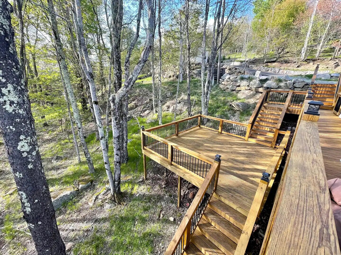 A wooden deck with a railing, surrounded by trees and a rocky landscape.