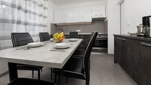 A modern kitchen with white cabinets, a grey countertop, and a dining area with a grey table and black chairs.