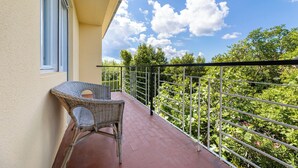 A balcony with a wicker chair, a metal railing, and a view of green trees and a clear sky.