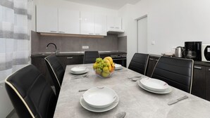 A modern kitchen with white cabinets, a dining table with black chairs, and a fruit bowl on the table.