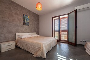 Un dormitorio con cama, mesita de noche, un cuadro en la pared y una puerta corrediza de vidrio que da a un balcón.