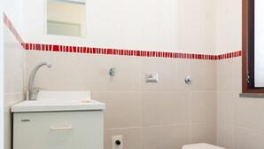 Un baño con un lavamanos blanco, un inodoro y un espejo sobre el lavamanos.