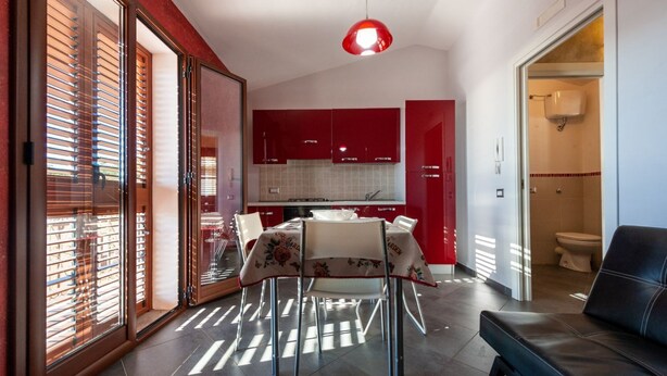 Una cocina moderna con armarios rojos, una mesa de comedor con sillas y un sofá de cuero negro en una sala de estar.