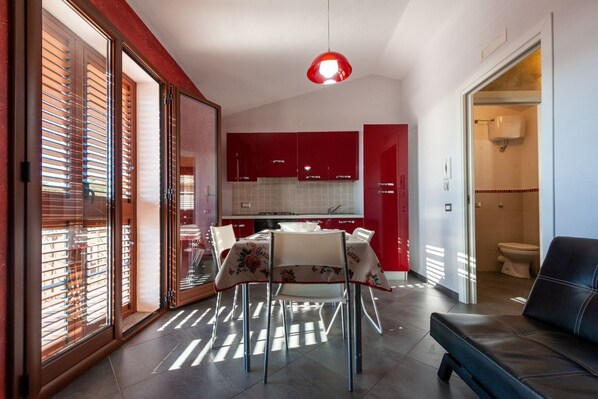 Una cocina moderna con armarios rojos, una mesa de comedor con sillas y un sofá de cuero negro en una sala de estar.