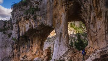 A natural rock formation with a large archway and a person standing at the base.