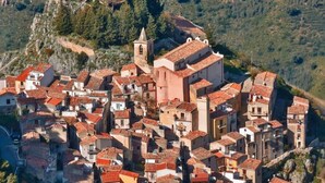 Un pueblo en una ladera densamente poblada, con arquitectura tradicional, incluyendo edificios con tejados de tejas y una iglesia destacada con un campanario.