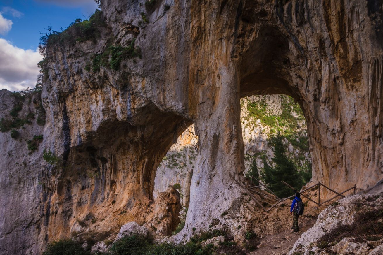 A natural rock formation with a large archway and a person standing at the base.