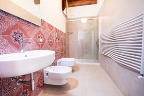 A bathroom with a white sink, two toilets, and a glass shower enclosure.