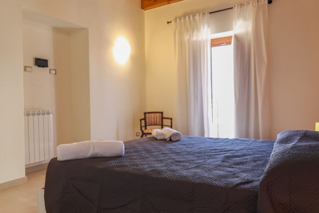 A bedroom with a bed, a chair, and a window with curtains.