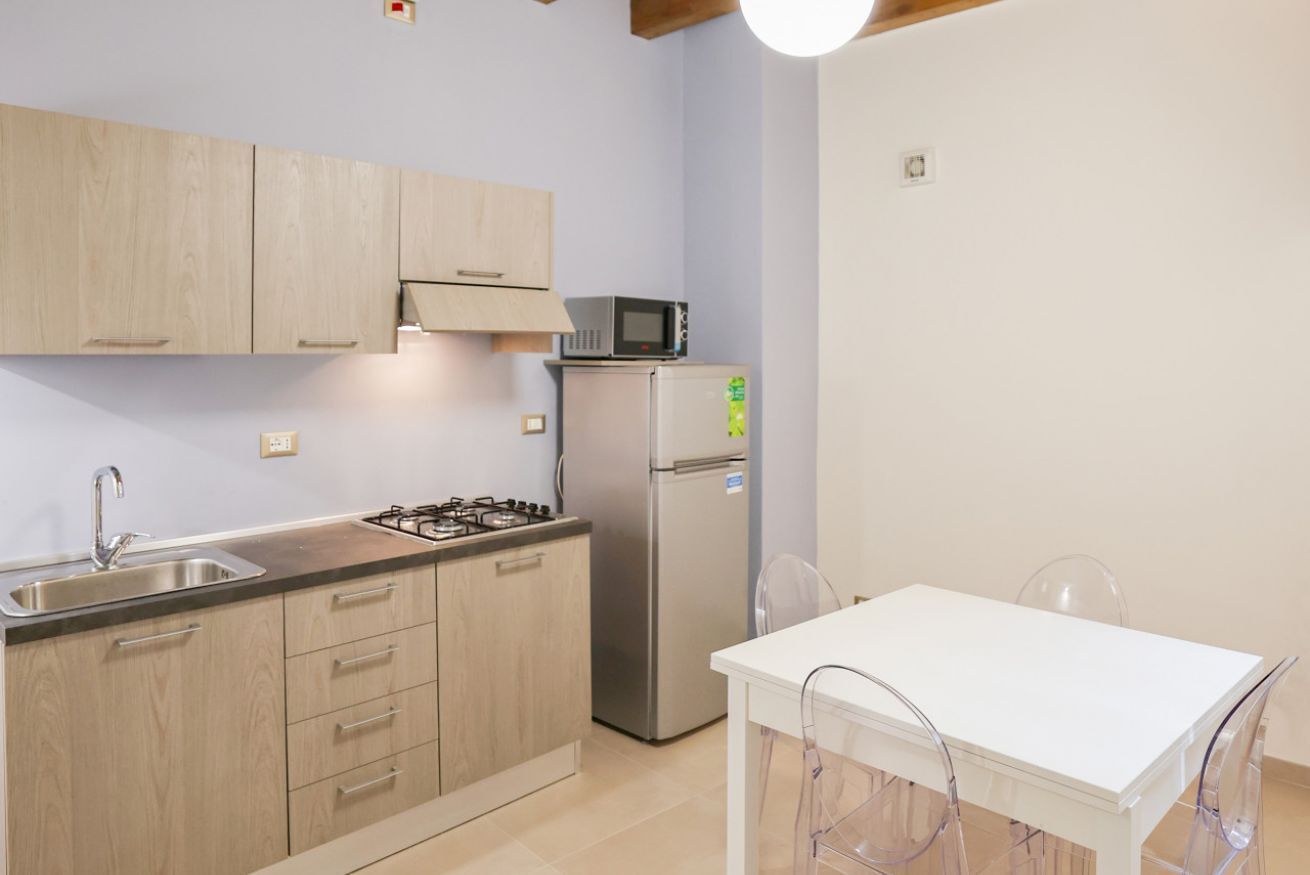 Une cuisine de taille réduite, dotée de meubles en bois, d’une cuisinière à gaz, d’un four à micro-ondes et d’un réfrigérateur.